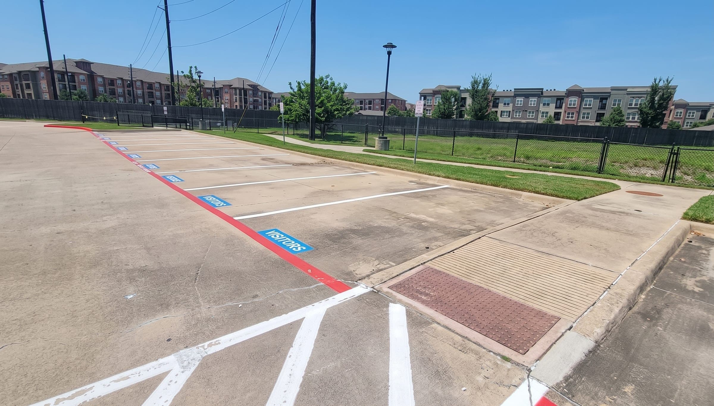 Pintura nueva en el estacionamiento de un complejo de apartamentos: líneas blancas de cajones, esténciles azules de VISITORS y un bordillo rojo de zona de bomberos